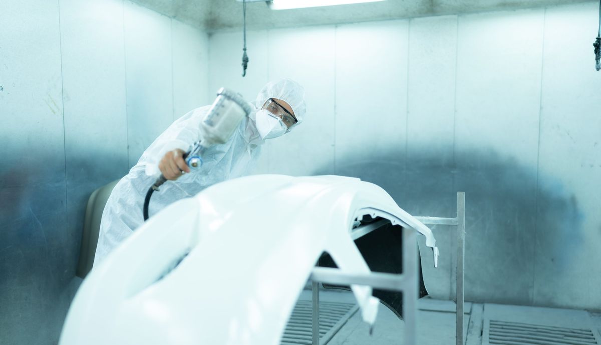 Technician inspecting a freshly coated part in the spray booth