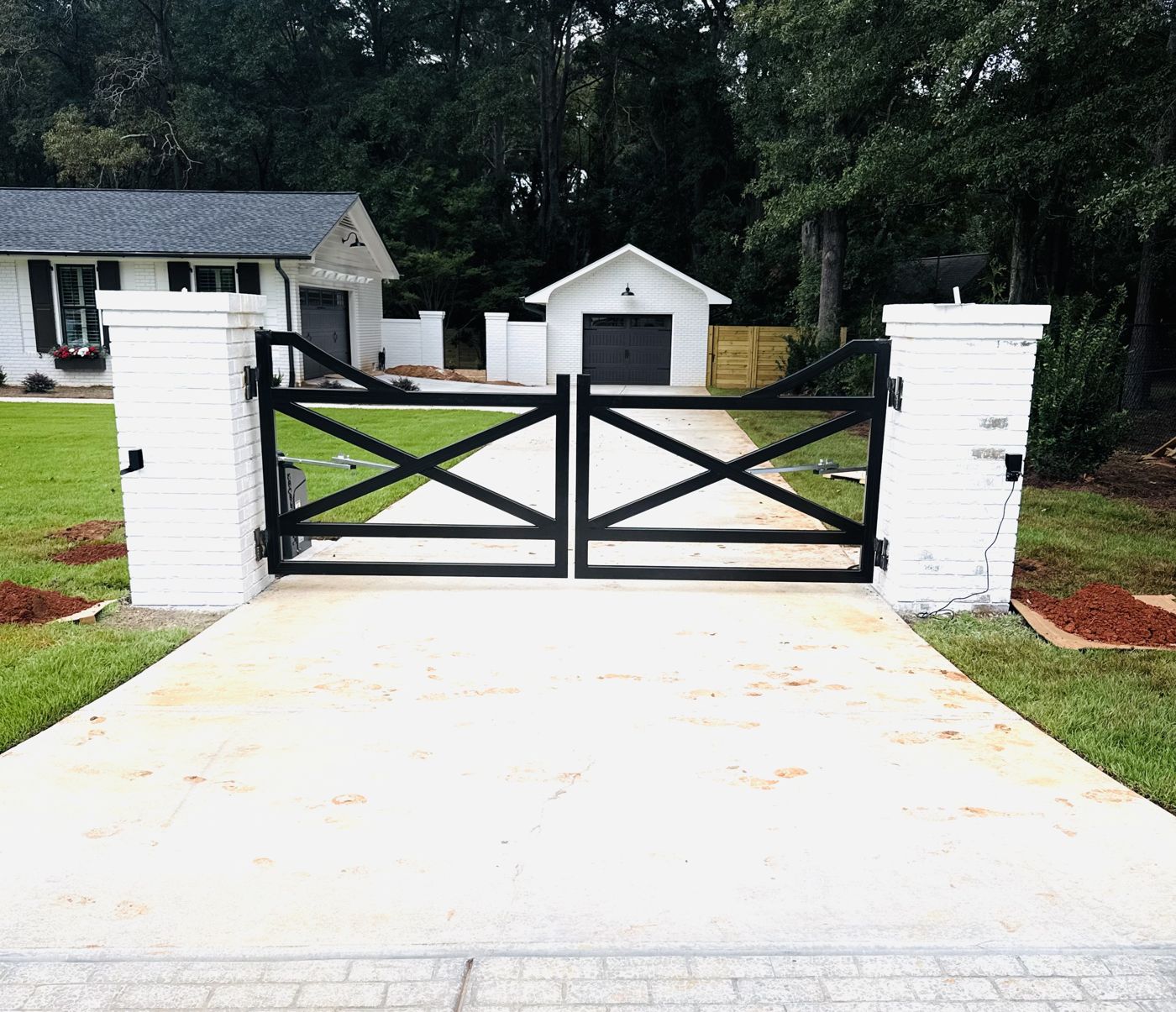 Powder coated black double driveway gate between white brick columns